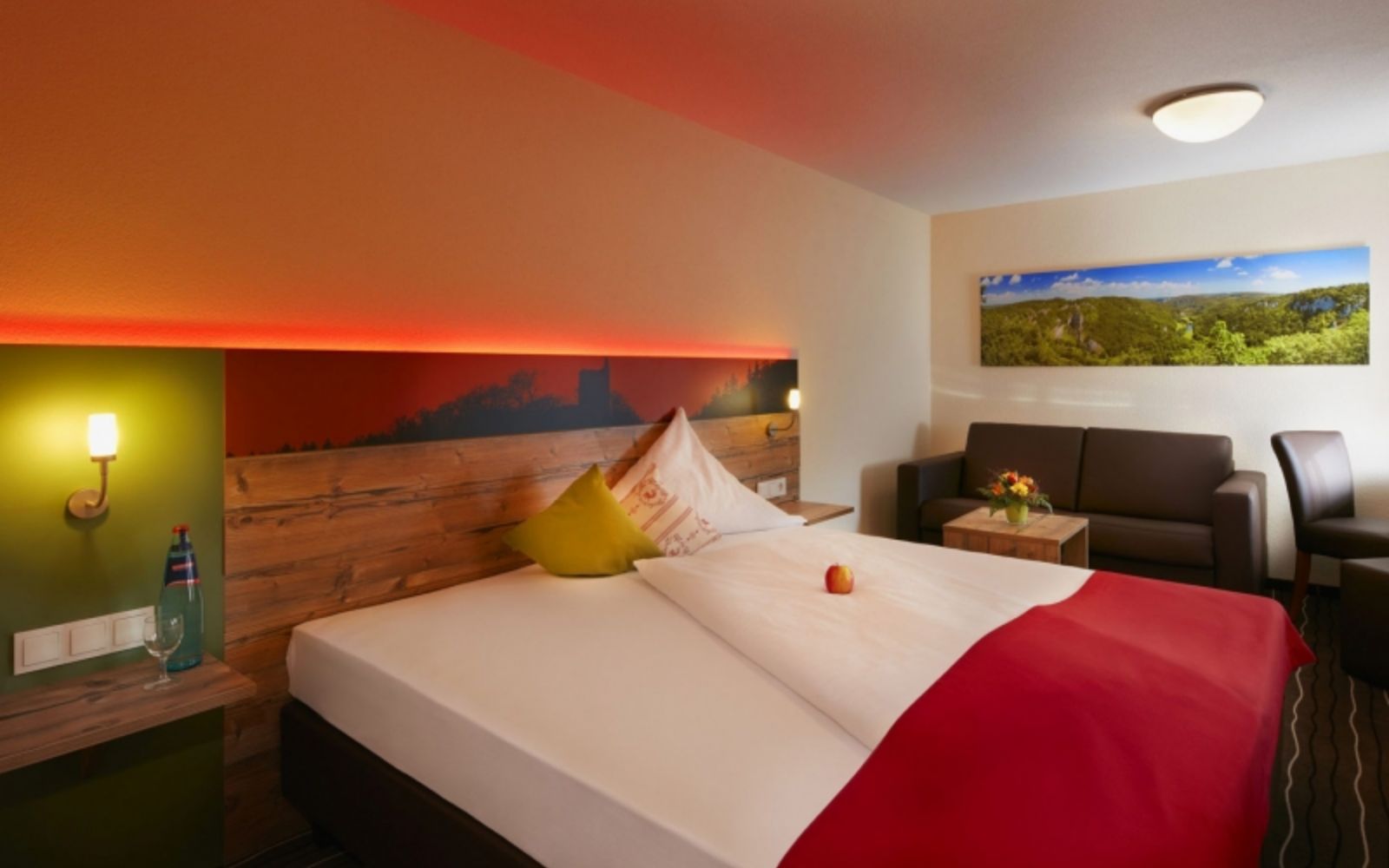 Themenbild von einem Hotelbett in einem modernen Zimmer mit brauner Ledercouch und roter Hintergrundbeleuchtung am Bett