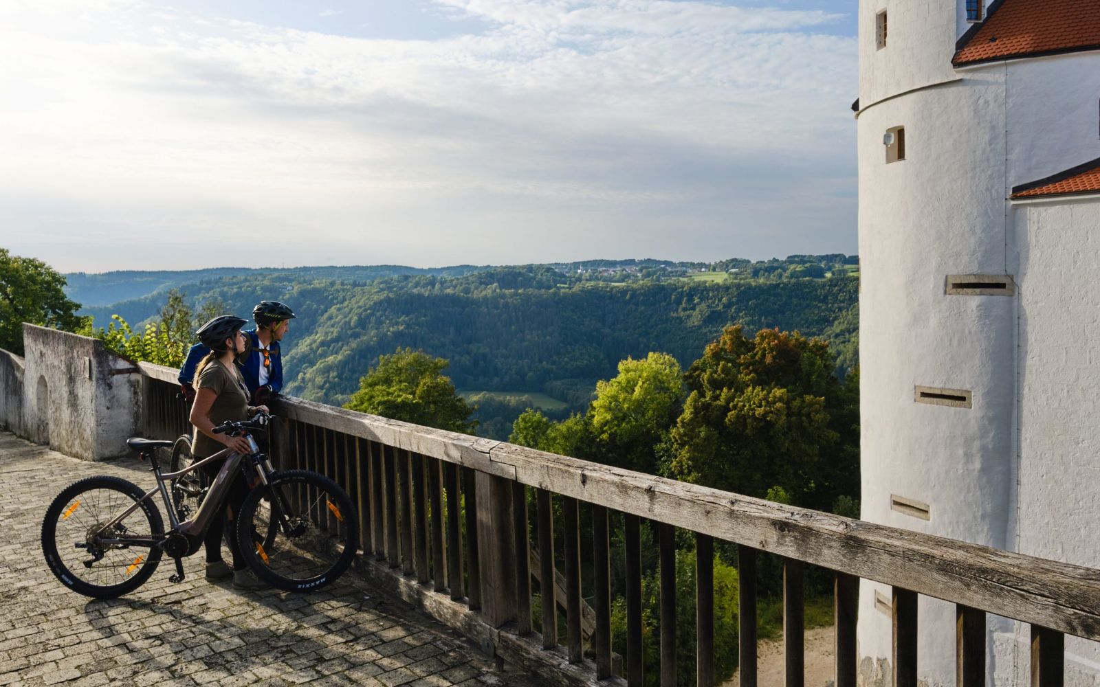 Themenbild mit zwei Radfahrern, die am Geländer vor Burg Wildenstein in die Natur schauen