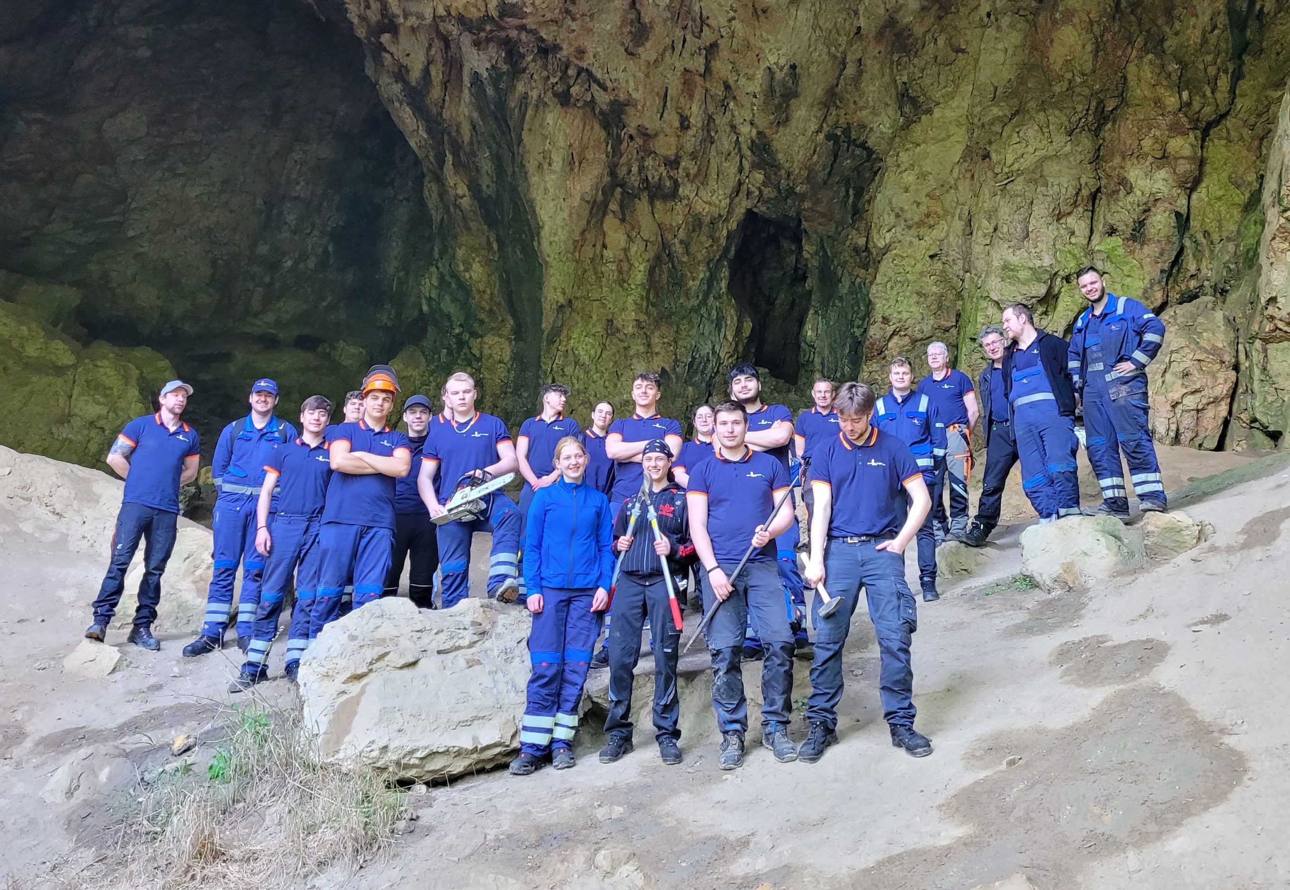 Bild von Azubis der Firma Hammerwerk vor einer Höhle, alle komplett blau gekleidet