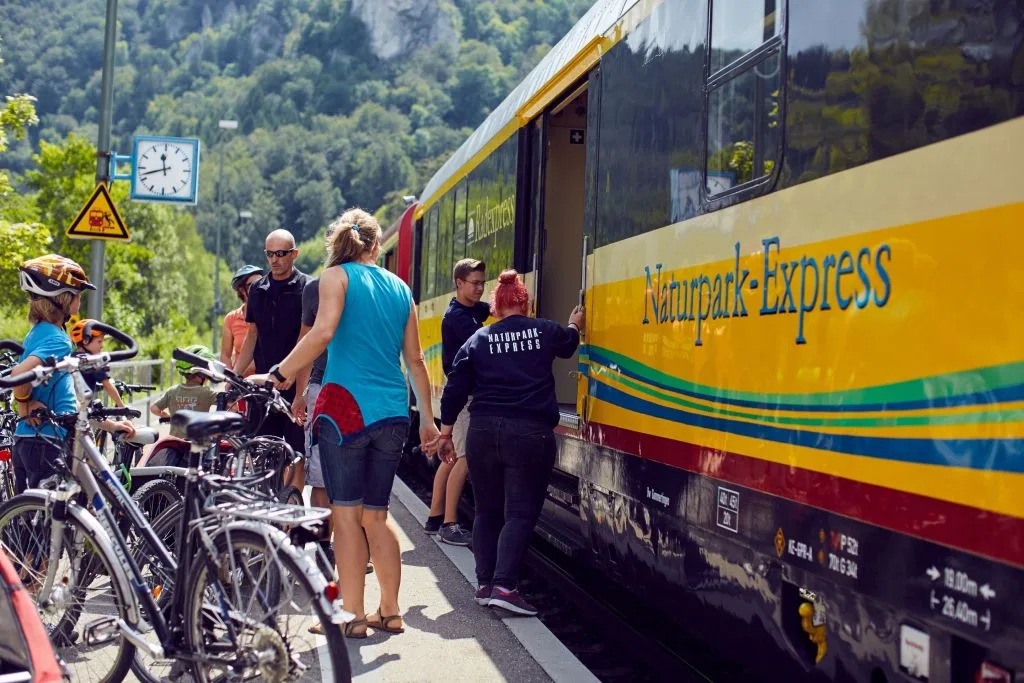 Bild von Fahrradfahrern, die vor dem Naturpark-Express stehen und einsteigen wollen. Die Uhr am Bahnsteig zeigt 11.42 Uhr an.