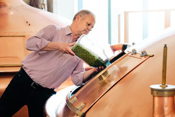 Bild von einem Bierbraumeister in der Hirschbrauerei, der gerade aus einem großen Glas grüne Zusätze in den Braukessel füllt