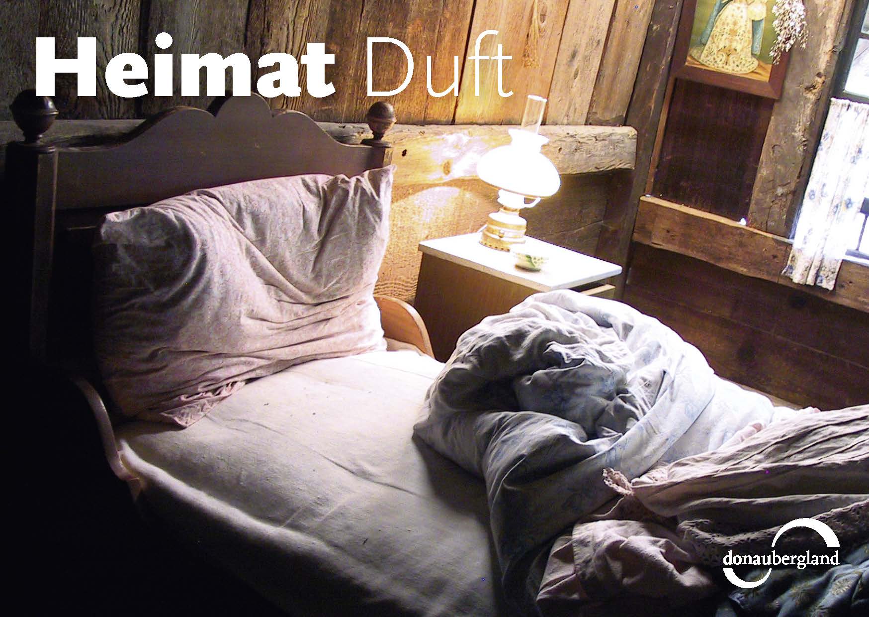 Donaubergland Postkartenmotiv mit Bett mit zurückgeschlagener Decke in einem alten mit Balken errichteten Raum.