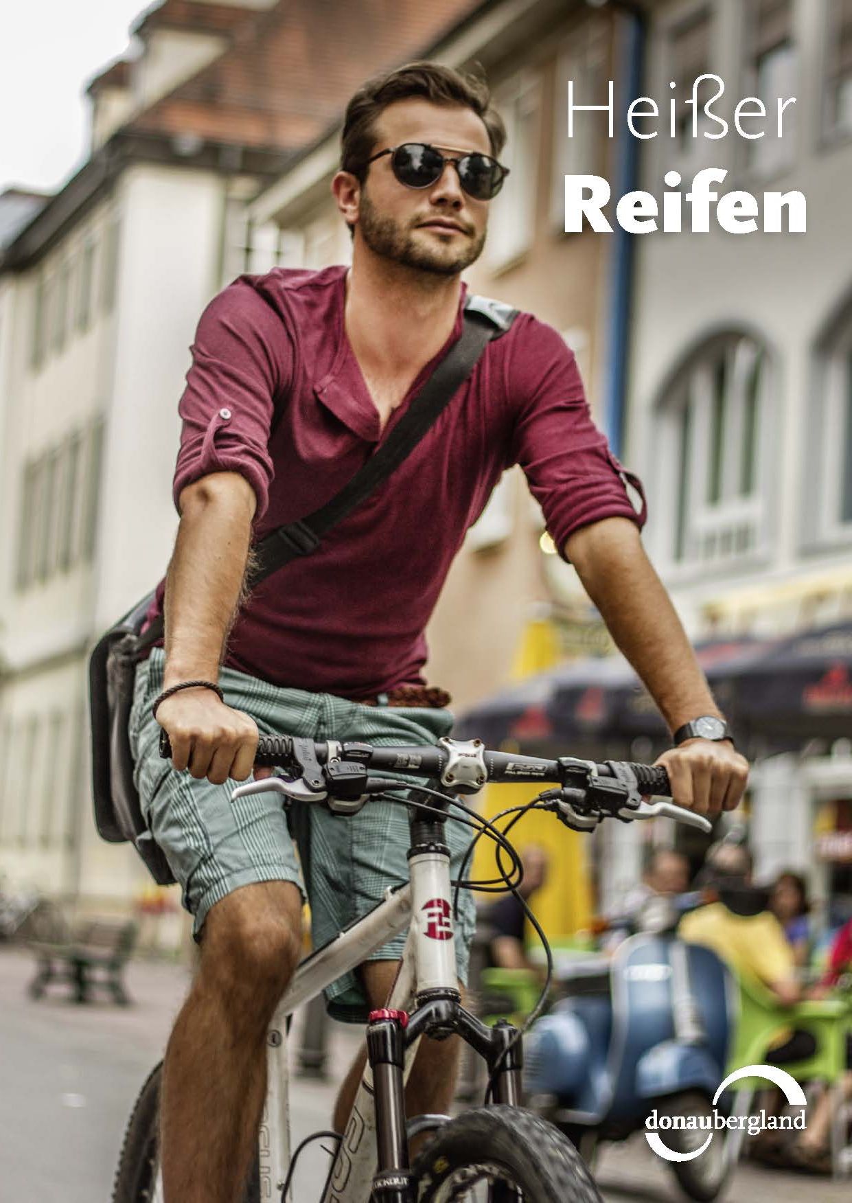 Donaubergland Postkartenmotiv mit Mann auf Fahrrad mit Umhängetasche fahrend durch Straße.