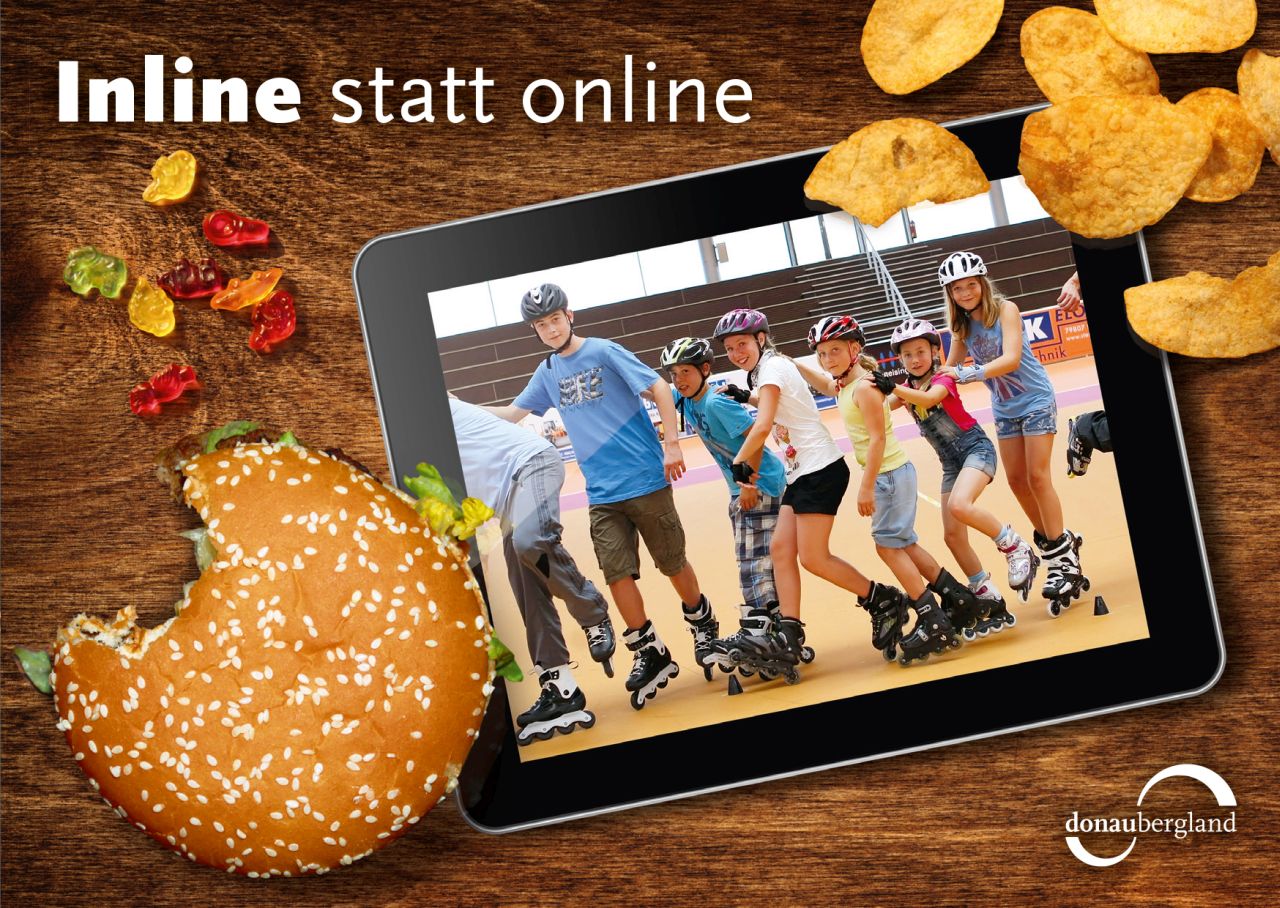 Donaubergland Postkartenmotiv mit Tablet auf Tisch mit Inline-Fahrern auf Bildschirm und angebissener Burger, Gummibärchen und Chips auf dem Tisch.