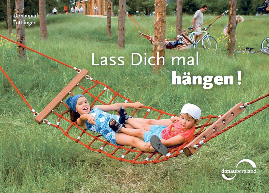 Kinder, die auf einer Wiese zwischen Bäumen in einer Hängematte liegend sich freuen