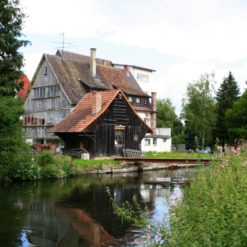 Bild von einem alten Gebäude, der Stadtmühle in Geisingen von hinten, am Wasser gelegen, eingesäumt von Wiesen und Bäumen