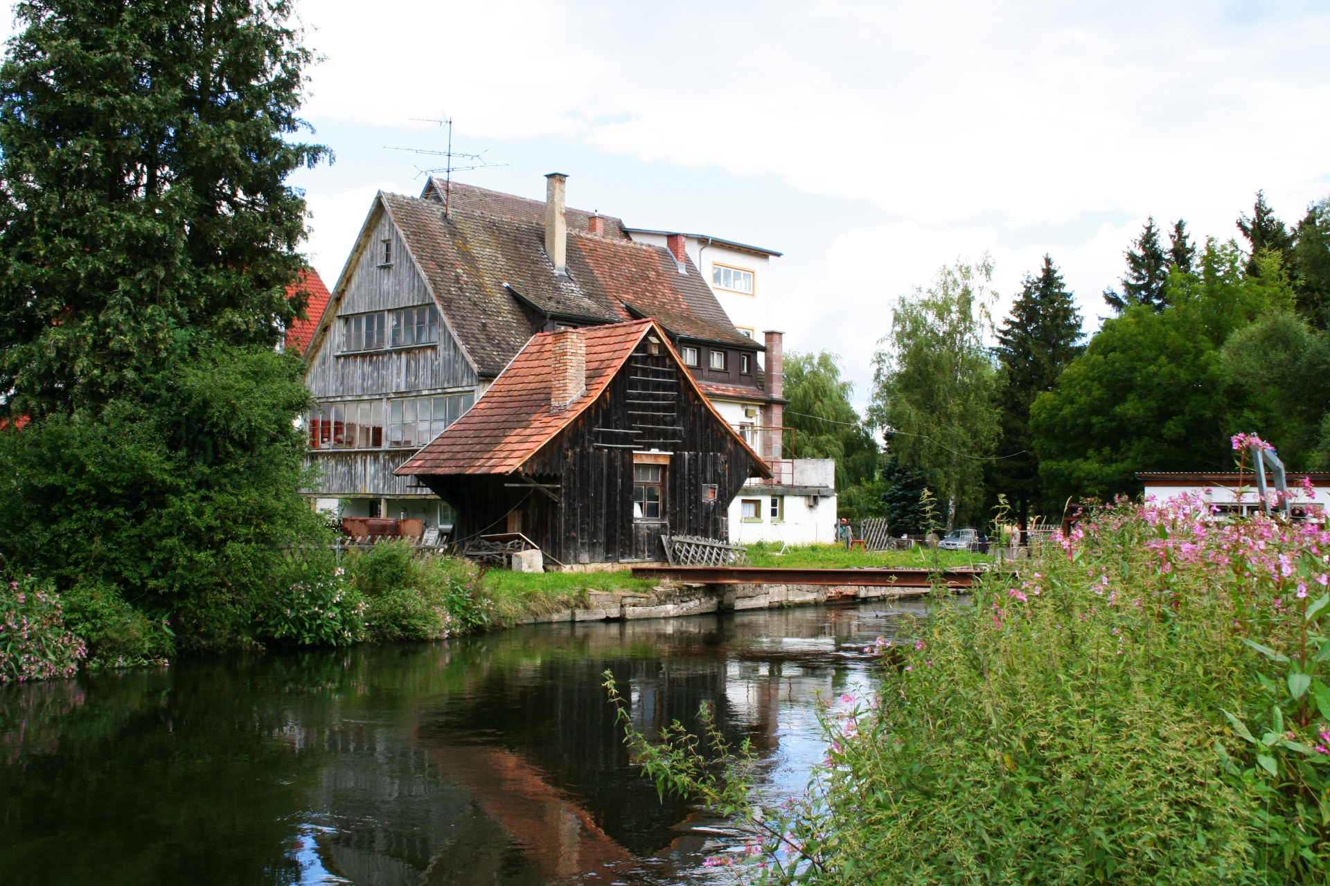 Bild von einem alten Gebäude, der Stadtmühle in Geisingen von hinten, am Wasser gelegen, eingesäumt von Wiesen und Bäumen