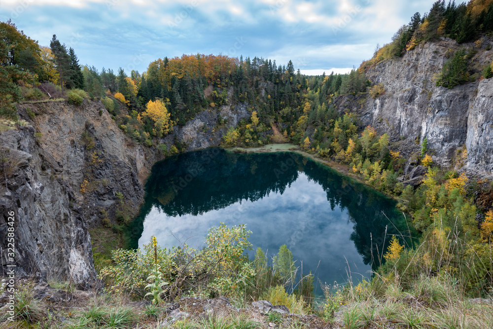 Bild auf einen Vulkankratersee in dem sich die herbstlichverfärbten Bäume und die Felsen spiegeln mit blauem Himmel im Hintergrund
