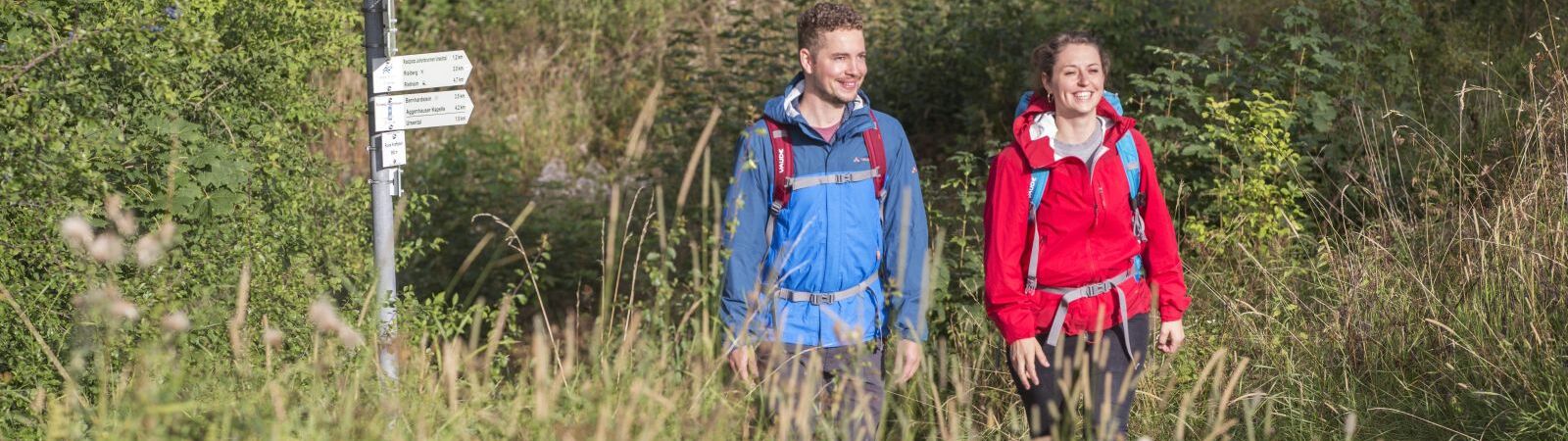 Bild von einem Wanderer und einer Wanderin, die im hohen Gras stehen und beide lächeln