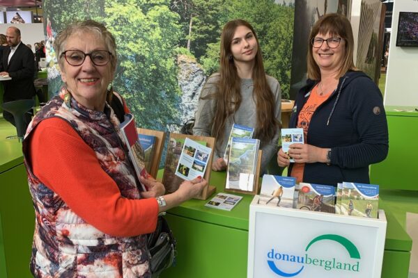 Foto von zwei Personen hinter Messestand und einer Person vor dem Messestand