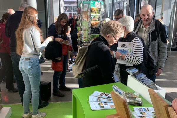 Foto von Personen auf Messestand, die Prospekte und Karten anschauen.