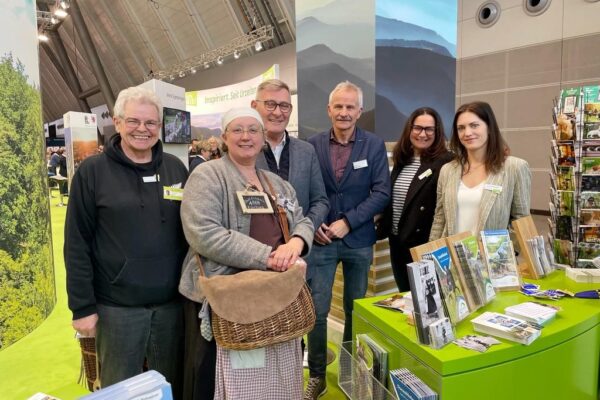 Foto von 6 Personen hinter Messestand mit Prospekten und Postkarten im Vordergrund