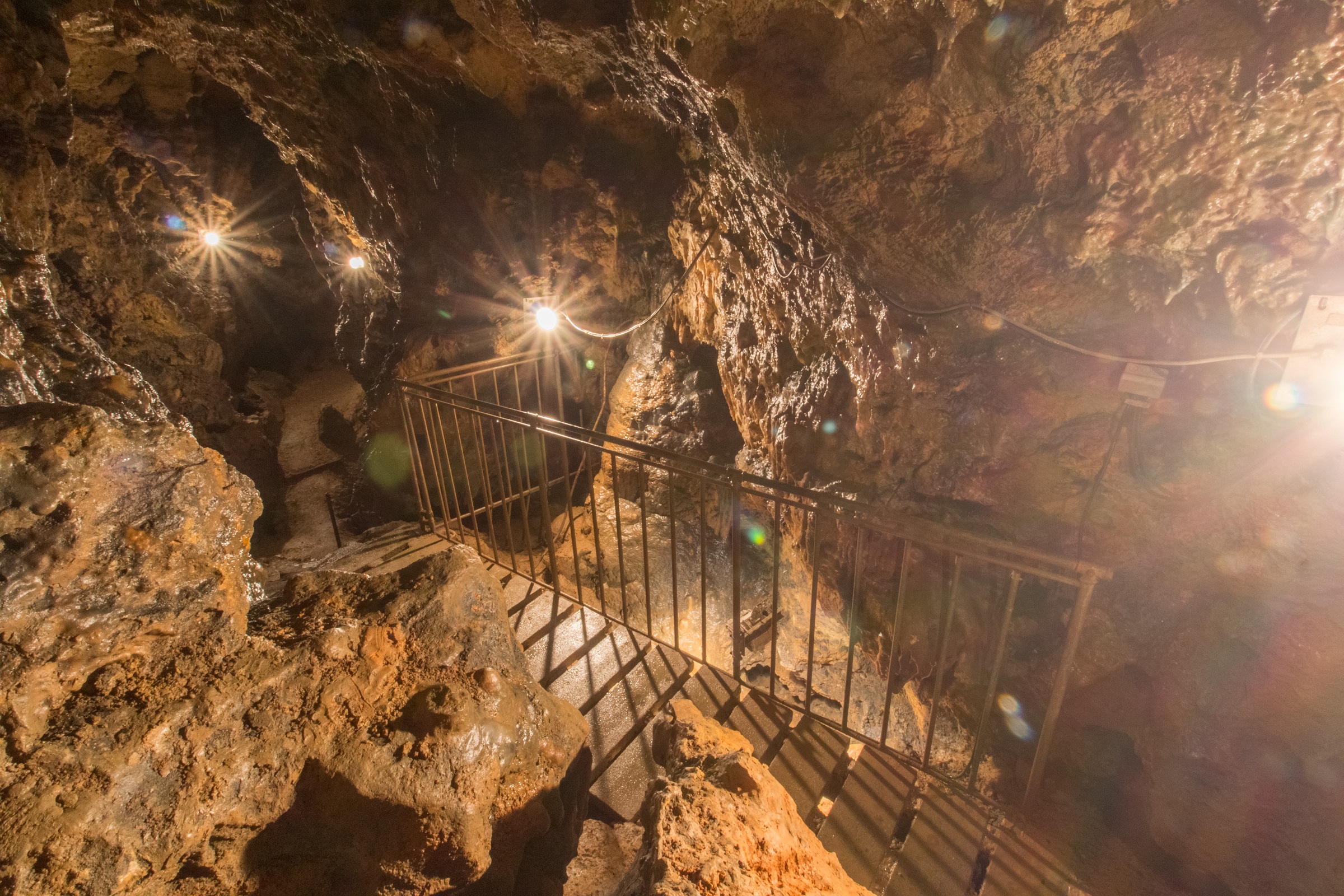 Bild von der Felsenhöhle von Innen mit einem beleuchteten Weg auf Holzdielen an einem Eisengeländer entlang