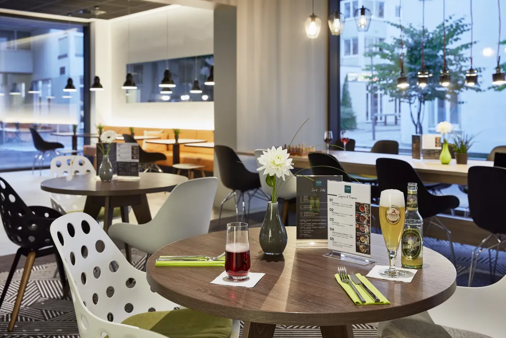 Bild mit Ausschnitt einer Gaststätte mit kleinen Tischen mit Getränken, Blumen und Speisekarten