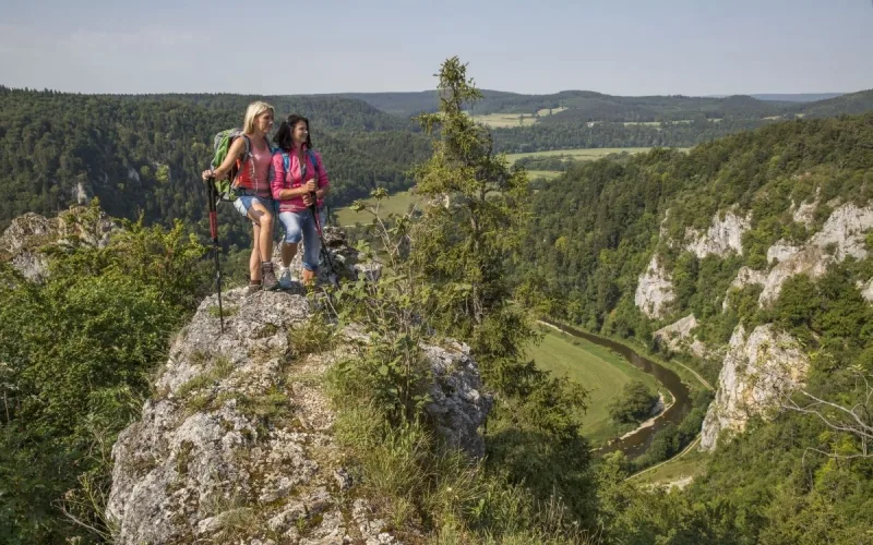 Bild von zwei Wanderinnen, die auf einem Felsen stehend die Aussicht ins Donaubergland genießen