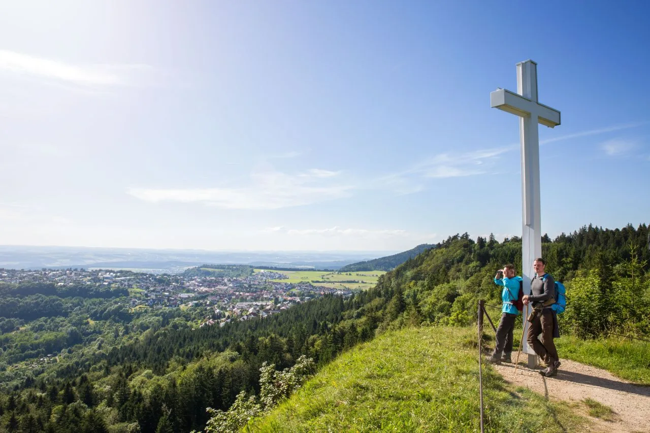 Bild von zwei Wanderern, die am Weißen Kreuz lehnen und die Aussicht genießen