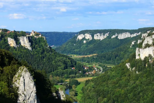 Bild ,mit Blick auf die Eichfelsen umsäumt mit bewaldeten Hügeln und im Tal ein Dorf und die Donau