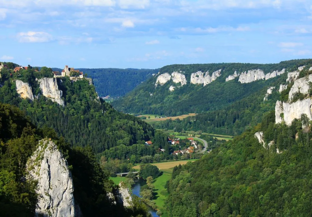 Bild ,mit Blick auf die Eichfelsen umsäumt mit bewaldeten Hügeln und im Tal ein Dorf und die Donau