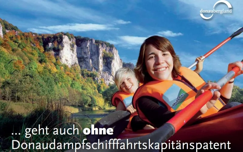 Bild der Donaubergland Postkarte mit dem Schriftzug ... geht auch ohne Donaudampfschifffahrtskapitänspatent mit zwei Frauen in einem Kajak vor einem Felsen auf der Donau