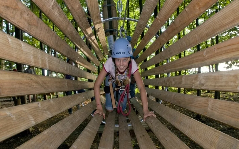 Bild von einem Kind in einer Holzröhre mit Kletterausrüstung im Hirscherlebniswald in Mahlstetten