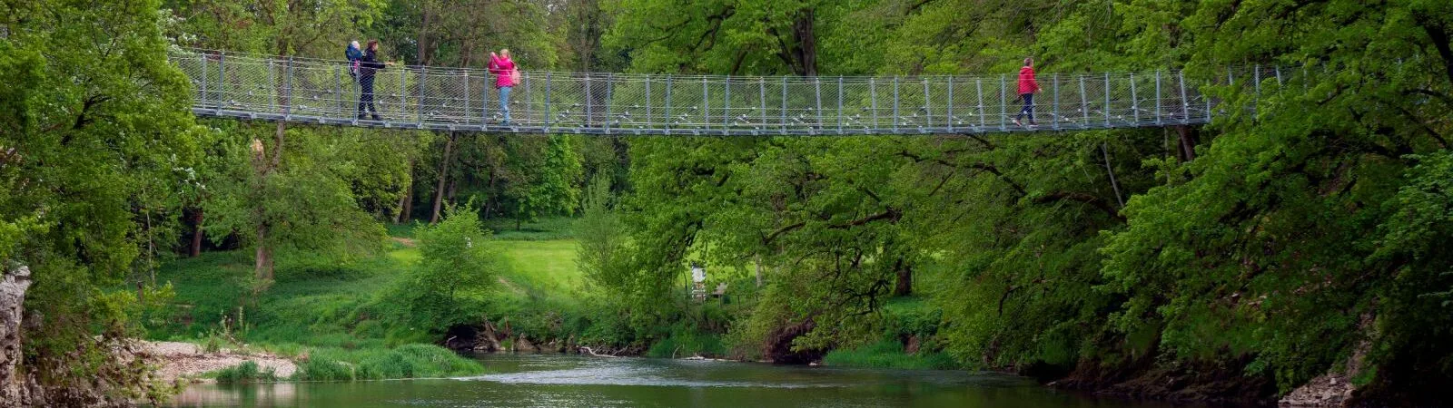 Bild von Hängebrücke über Wasser mit 4 Personen auf der Brücke