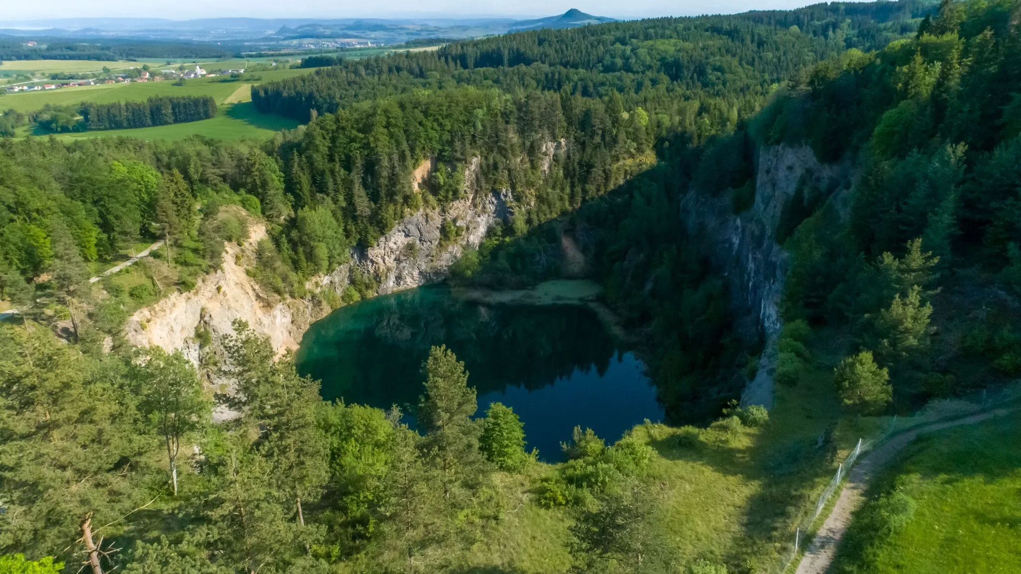 Bild von Blick auf den Kratersee Höwenegg von oben eingebettet in Felsen, Bäumen und Feldern