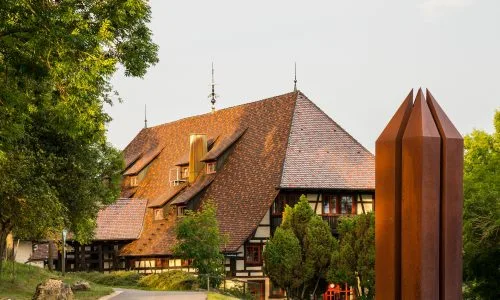 Bild von der Front des Hotel Hofgut Hohenkarpfen mit Rostskulptur rechts im Vordergrund