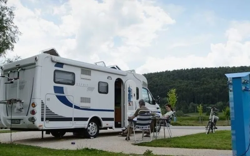 Bild von einem Camper auf dem Reisemobilstellplatz in Geisingen. Zwei Personen sitzen neben Ihrem Camper und lesen. Der Himmel ist bewölkt