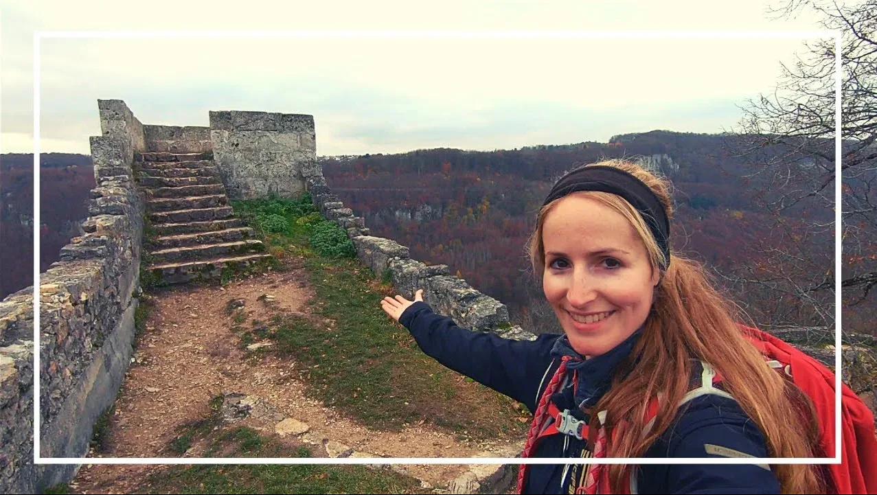 Videovorschaubild mit einer Wanderin mit Stirnband vor einer Steintreppe mit bewaldeten Hügeln mit Herbstfärbung im Hintergrund