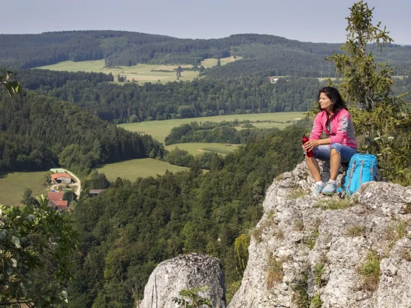 Bild einer Wanderin, die auf einem Felsen sitzt und in die Landschaft schaut