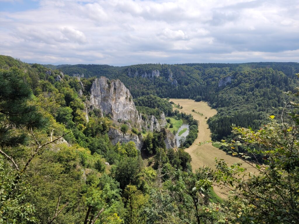 Blick von oben in ein Flusstal bewaldeten Hängen und einem großem Felsmassiv.