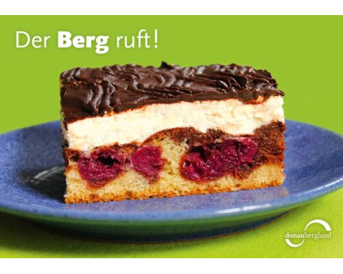 Donaubergland Postkartenmotiv mit einem Stück Donauwellen-Torte auf blauem Teller.