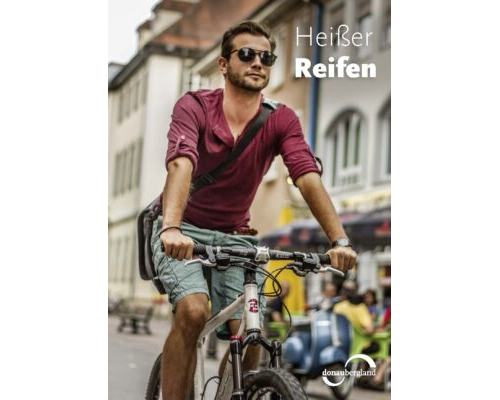 Donaubergland Postkartenmotiv mit Mann auf Fahrrad mit Umhängetasche fahrend durch Straße.