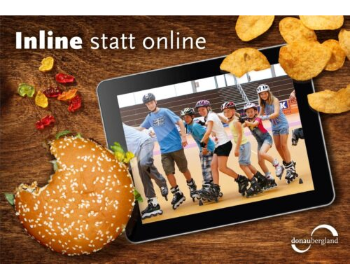 Donaubergland Postkartenmotiv mit Tablet auf Tisch mit Inline-Fahrern auf Bildschirm und angebissener Burger, Gummibärchen und Chips auf dem Tisch.