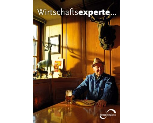 Donaubergland Postkartenmotiv mit Mann mit Hut in einer Wirtschaft mit Vesperbrett und Bier vor sich und über Ihm hängt ein Hirschgeweih und auf dem Fenstersims stehen ebenfalls Hirsche in verschiedenen Größen